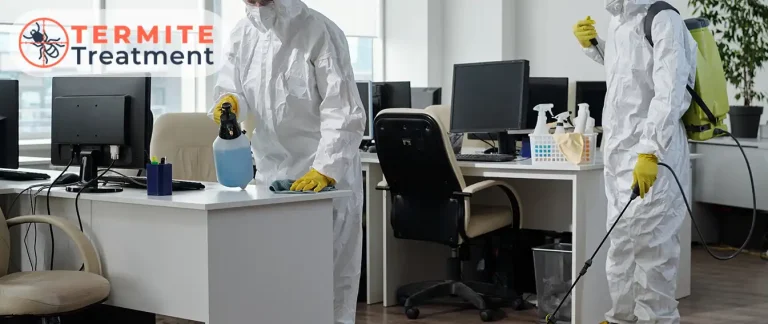 Professionals in protective gear applying termite treatment in an office setting.