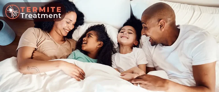 A happy family with two adults and two children lounging on a bed.