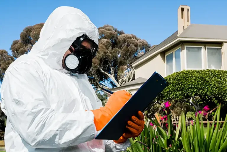 A person in a termite protection suit and mask holding a clipboard outside a residential building in Sydney.